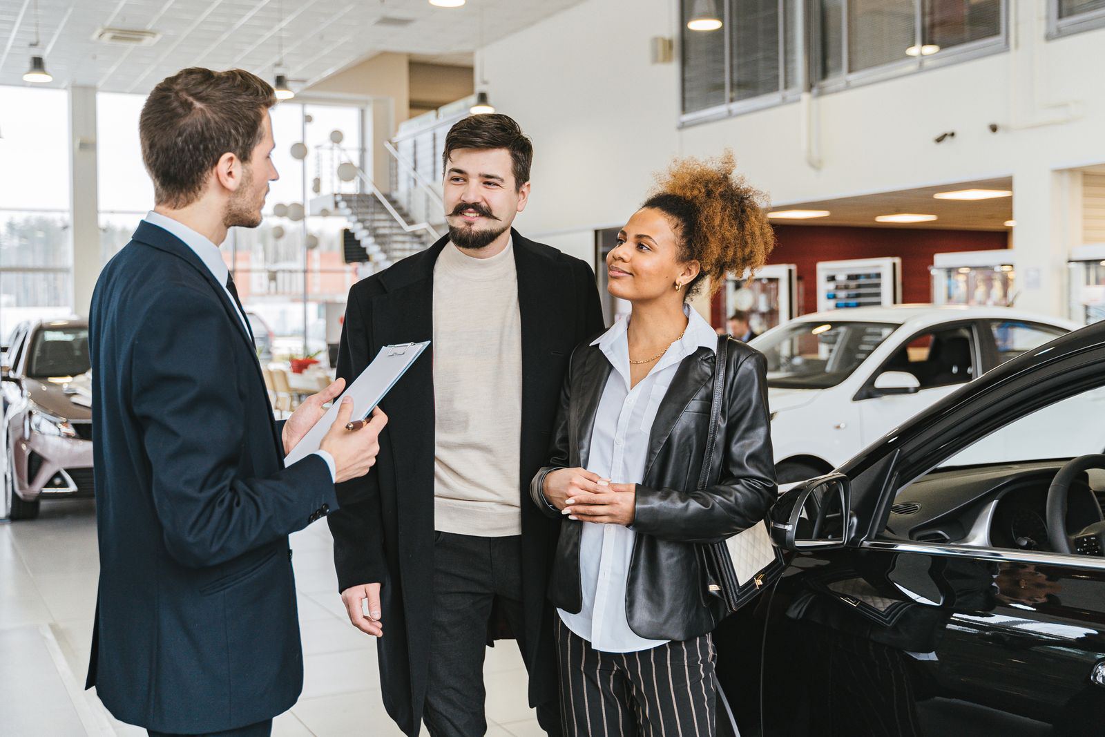 Two customers talking with a salesperson on a dealership floor